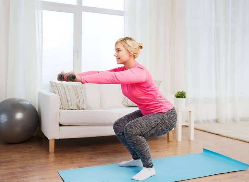 Lady doing squats on a yoga mat in her living room.