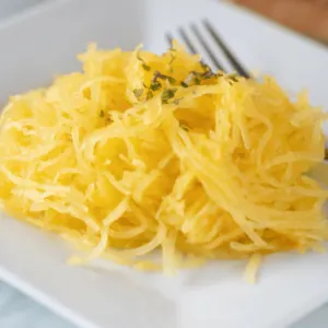 perfectly cooked spaghetti squash on white plate with fork ready to eat