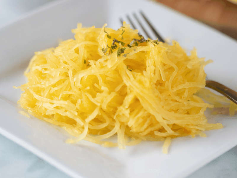 perfectly cooked spaghetti squash on white plate with fork ready to eat