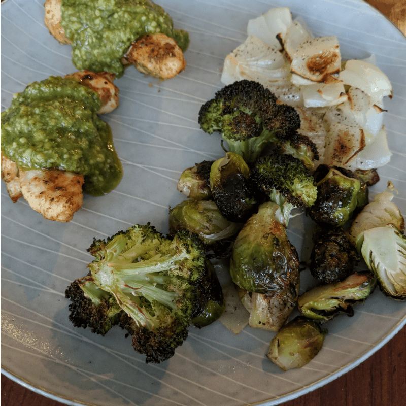 Dinner plate with air fried chicken tenders with basil pesto, roasted broccoli, onions and brussels sprouts.