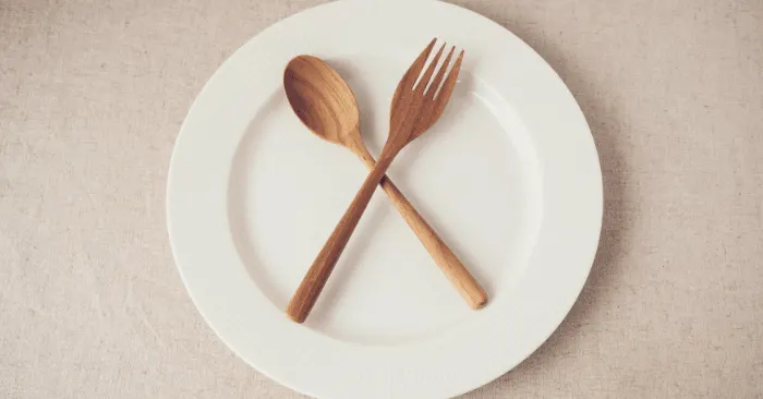 empty plate with fork and spoon laying on top during intermittent fasting