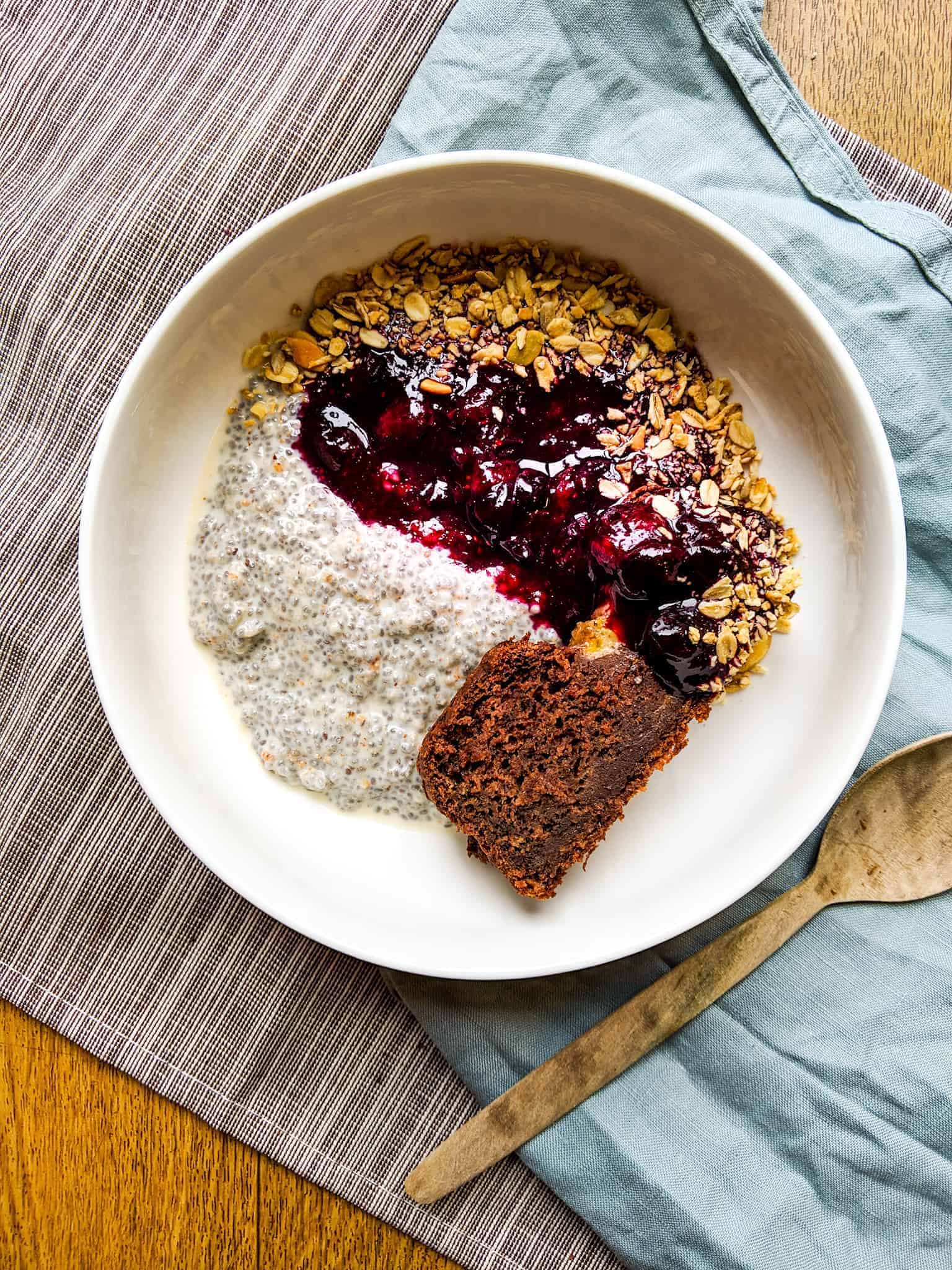chia seed pudding with stewed berries in a white bowl with a wooden spoon beside it