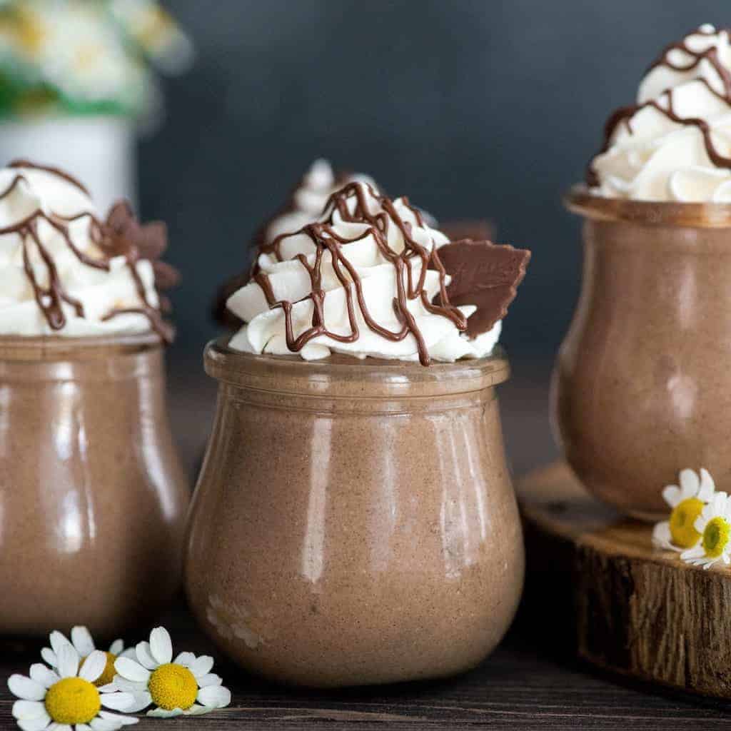 chocolate peanut butter chia pudding in clear jars with whipped cream topping and chocolate drizzled on top