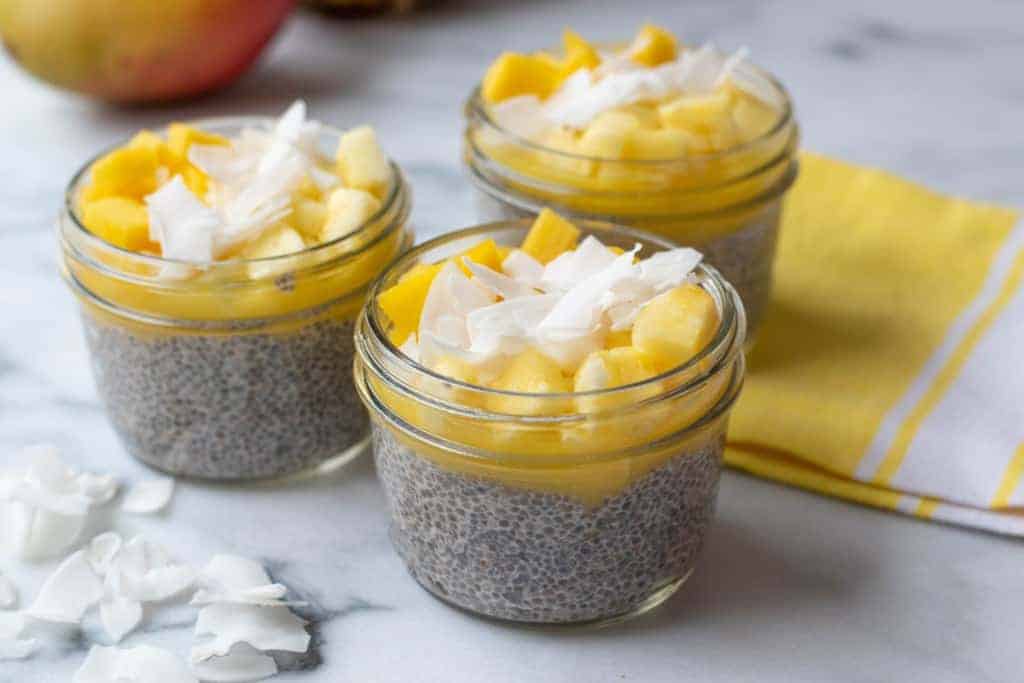 3 dishes with pineapple mango chia pudding with coconut flakes on top as garnish