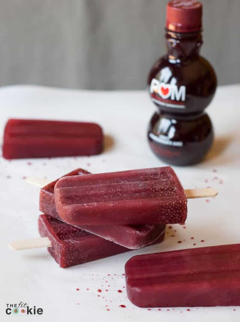 several pomegranate popsicles on a table beside POM juice