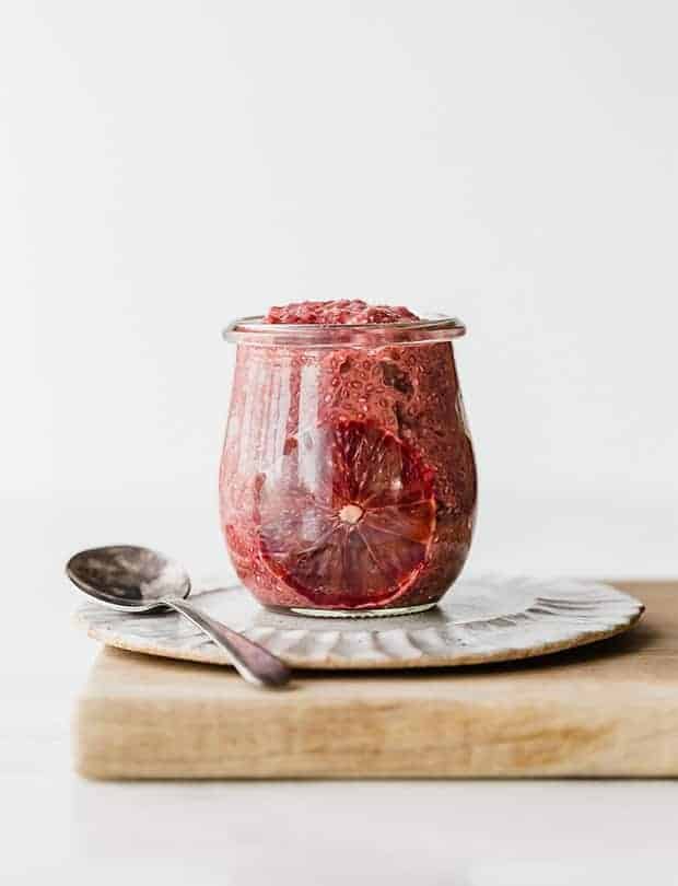 blood orange chia pudding in a glass jar with spoon sitting beside it