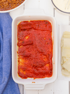 white lasagna pan with a light coating of spaghetti sauce on the bottom
