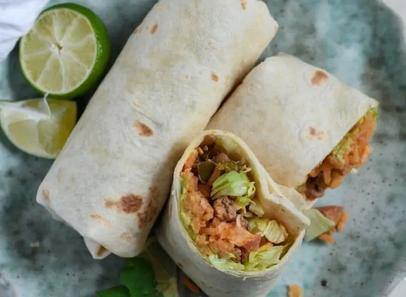 2 mexican burritos on a plate with one cut in half and a lime cut in half beside it