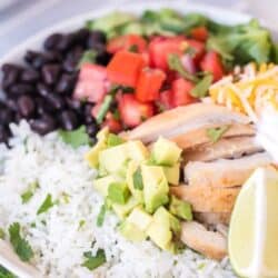 up close picture of rice bowl with burrito ingredients chicken sour cream, cheese, avocado, black beans, peppers and tomatoes