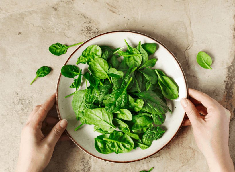 bowl of fresh spinach with a lady's hands holding the bowl