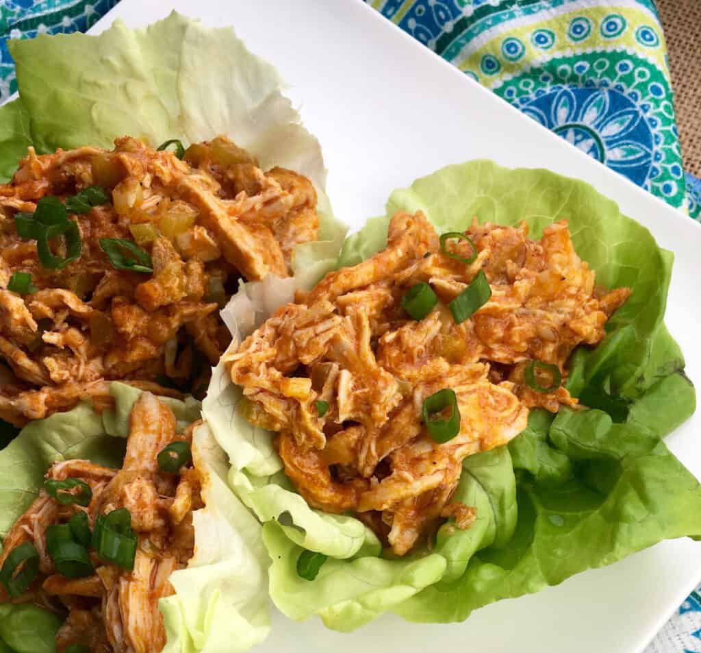 buffalo chicken in lettuce cups on a white plate with a blue decorative background