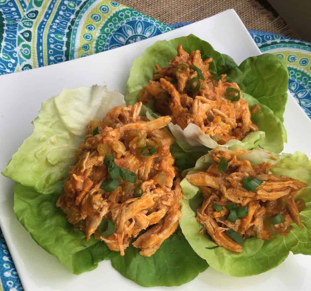 buffalo chicken in lettuce cups on a white plate with a blue decorative background