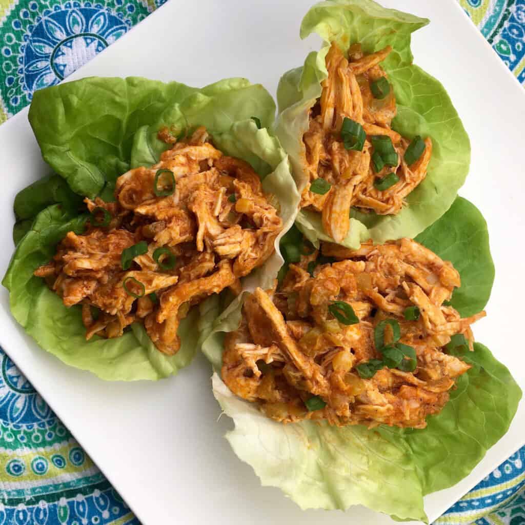 buffalo chicken in lettuce cups on a white plate with a blue decorative background