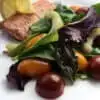 lemon dill salmon on a white plate with herbed salad and a lemon