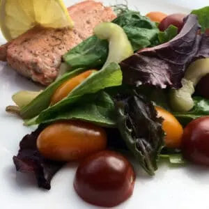 lemon dill salmon on a white plate with herbed salad and a lemon