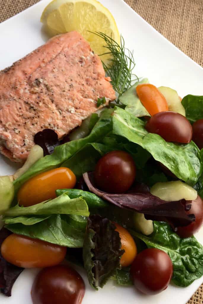 lemon dill salmon on a white plate with herbed salad and a lemon