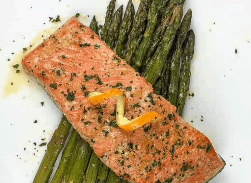 salmon with orange glaze and garnish on top of asparagus on a white plate