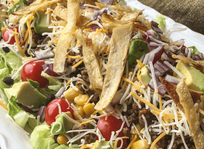 taco salad with ground beef veggies and tortilla strips on a large white platter