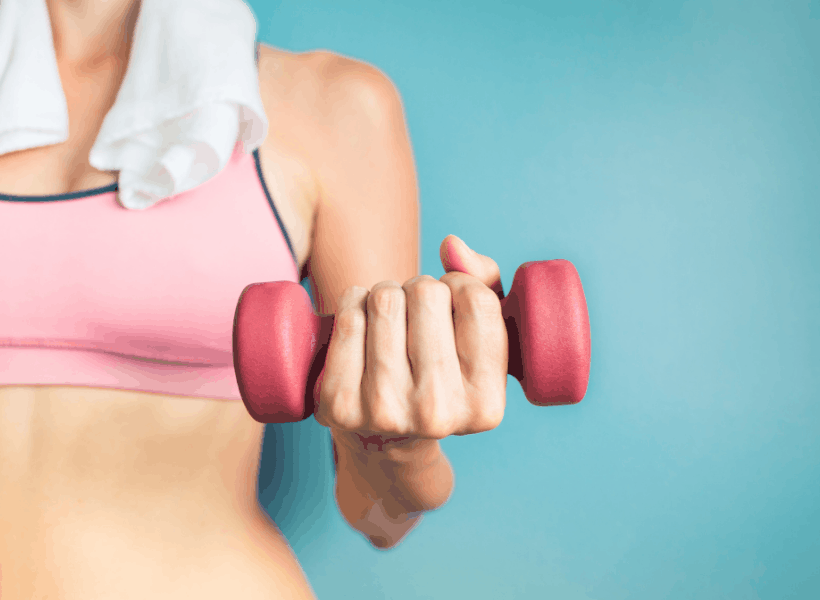 woman with sports bra on, towel around neck holding a dumbbell in hand while weight lifting