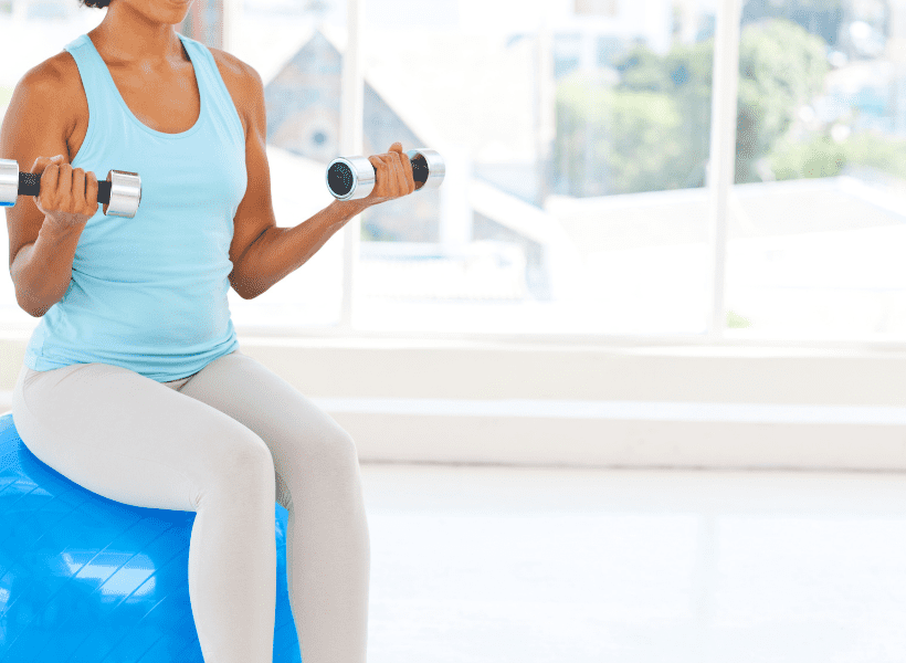 woman sitting on blue yoga ball with single dumbbells in each hand doing bicep curls