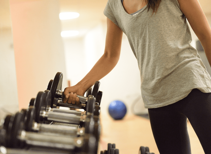 A thin lady taking a dumbbell from a rack of weights.