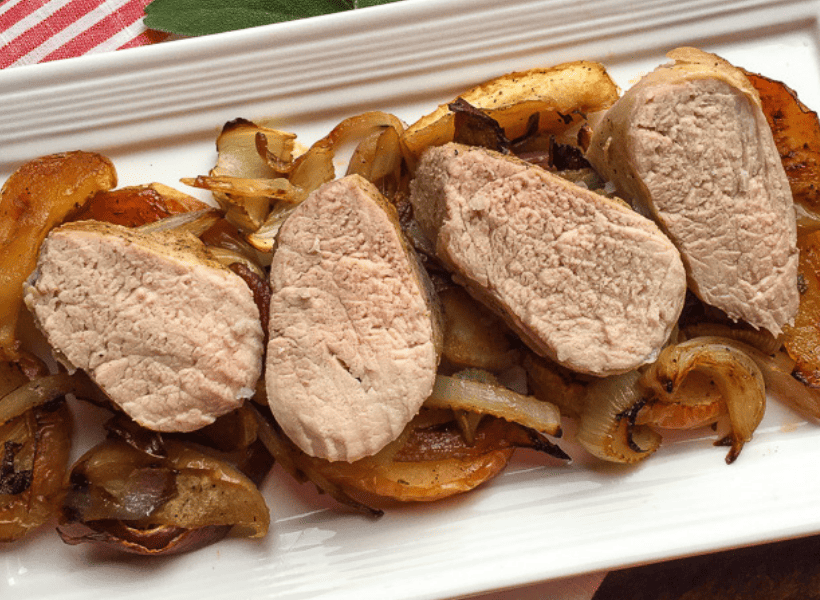 four pieces of sliced pork tenderloin laying on bed of roasted apples and fennel on a white serving plate