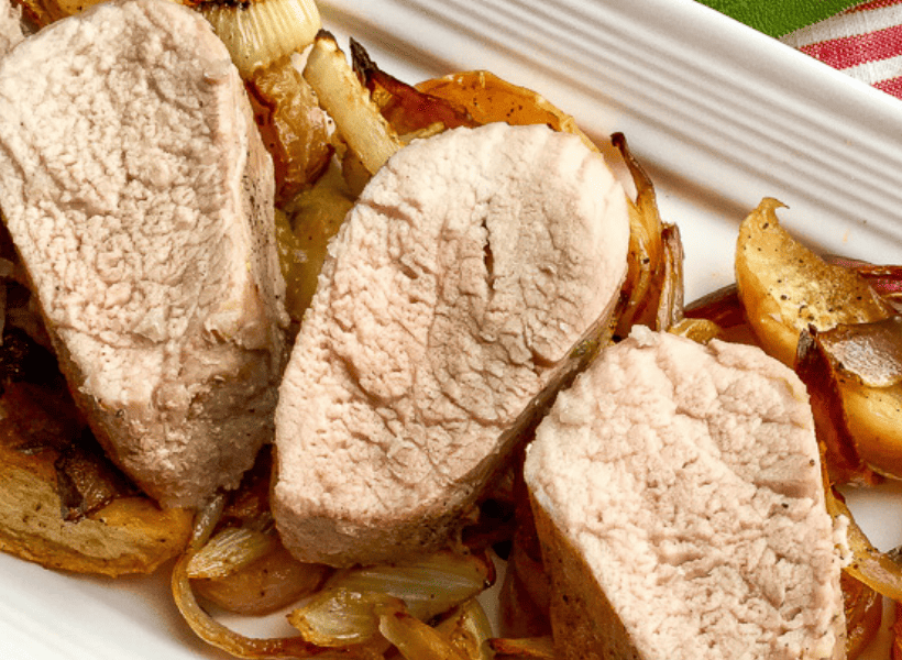 roasted pork tenderloin sliced laying on bed of fennel and apples all on a white serving plate