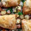 browned baked chicken thighs on sheet pan with herbs, red potatoes halved and sliced red onions