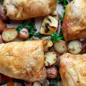 browned baked chicken thighs on sheet pan with herbs, red potatoes halved and sliced red onions