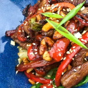 blue plate of stir fry with pork, bok choy and red peppers