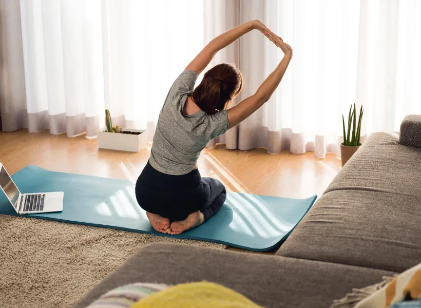 woman sitting on mat with back facing camera with arms overhead stretching to the right