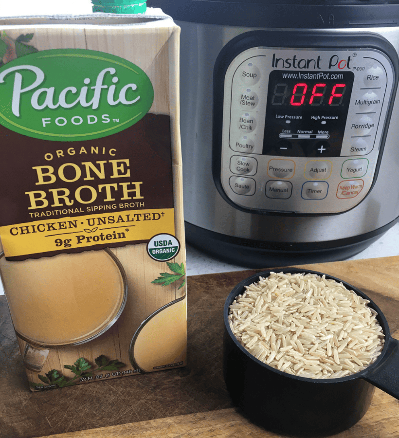 organic chicken bone broth box, an instant pot and a measuring cup of uncooked brown rice