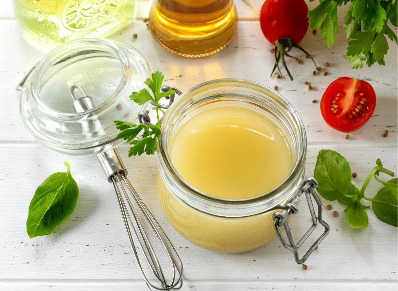Glass container of vinaigrette dressing with fresh tomatoes and herbs laying around it.