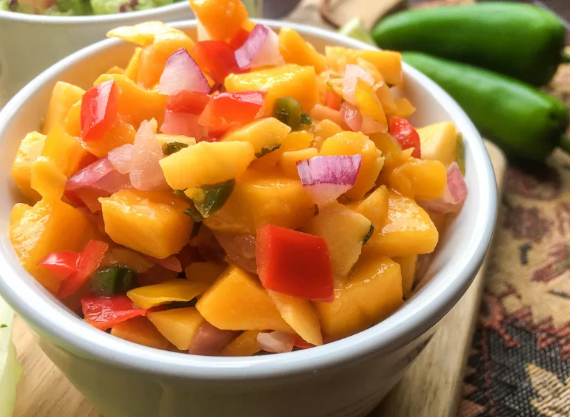 zoomed in image of mango peach salsa with red onion, jalapeno peppers and red bell peppers in a small white bowl
