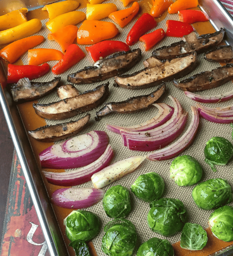 sheet pan and silpat with brussels sprouts, red onion, portobello mushrooms and mini peppers lined up ready to be roasted