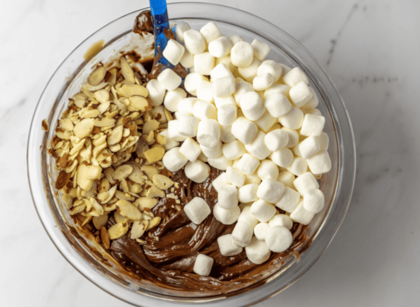 glass bowl with melted chocolate with marshmallows and almonds on top to be mixed together for rocky road fudge