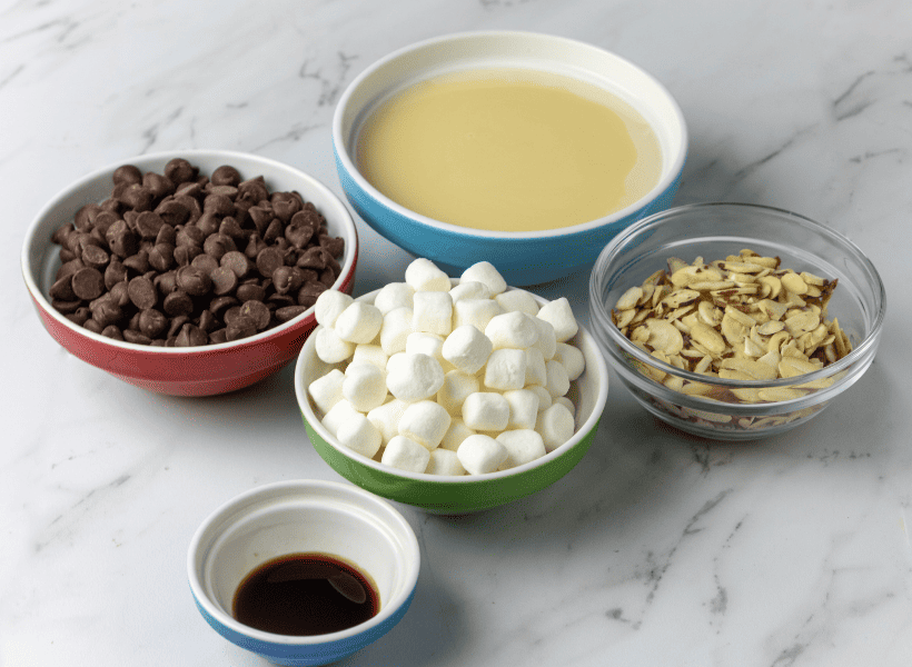 ingredients for rocky road fudge chocolate chips, marshmallows, sweetened condensed milk, almonds and vanilla in bowls