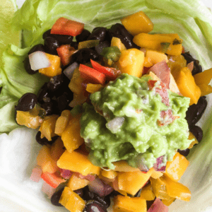 vegetarian lettuce wrap on a plate with black beans mango salsa guacamole on a white plate