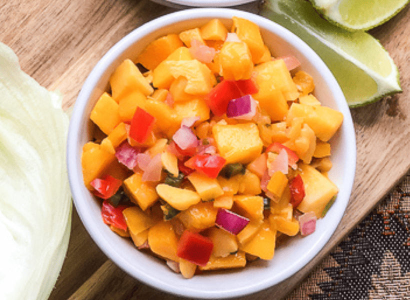 mango salsa with peppers and red onions in a white bowl on a wooden cutting board