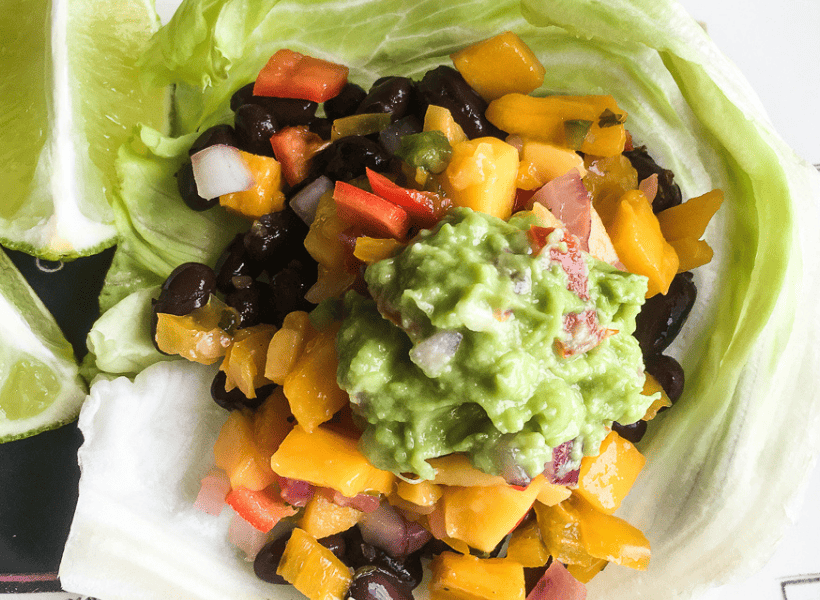 vegetarian lettuce wrap on a plate with black beans mango salsa guacamole on a white plate