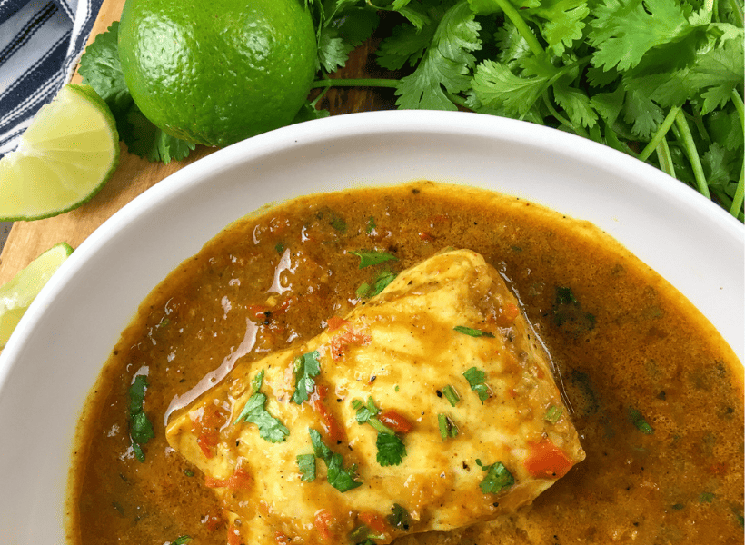 fish curry in white bowl with parsley and lime beside