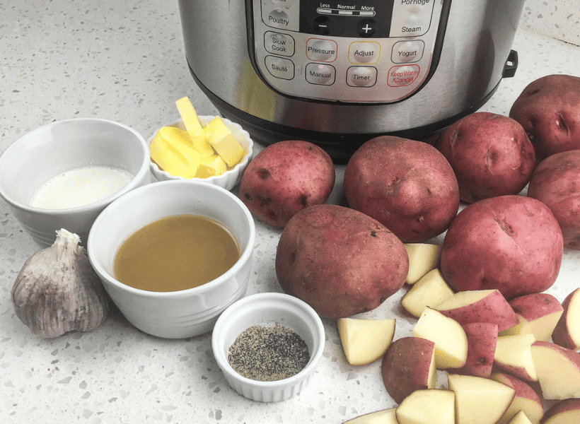 red potatoes, one potato cubed, bowls of ground pepper, chicken stock, heavy cream, garlic and butter on the counter next to an Instant Pot