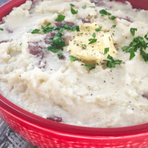red bowl of garlic mashed potatoes with butter and garnish