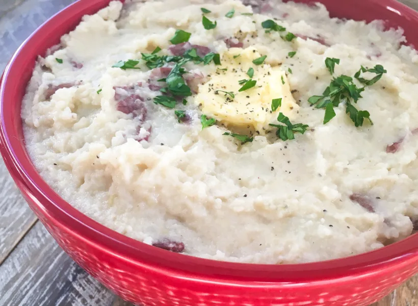 red bowl of garlic mashed potatoes with butter and garnish