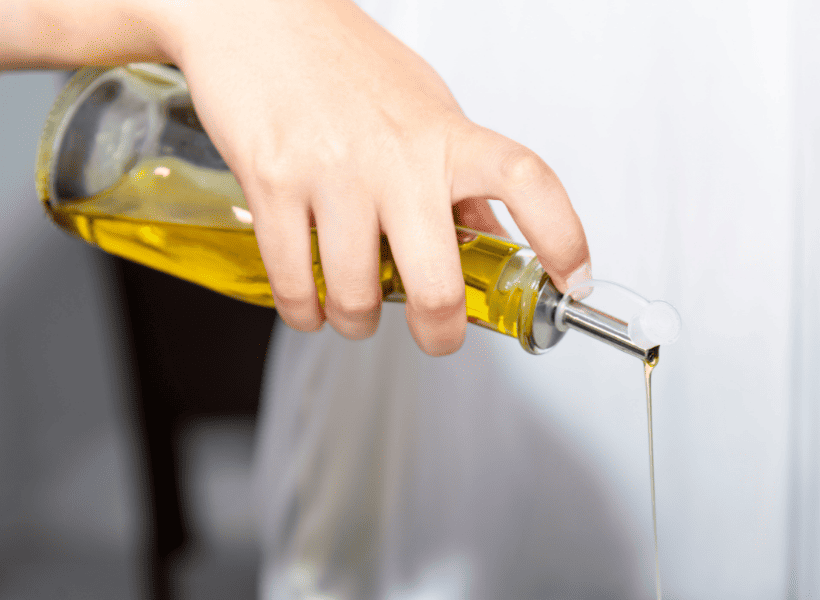person pouring olive oil out of a glass oil dispenser