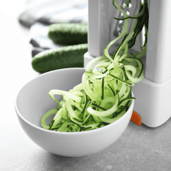 vegetable spiralizer cutting up zucchini into a white bowl