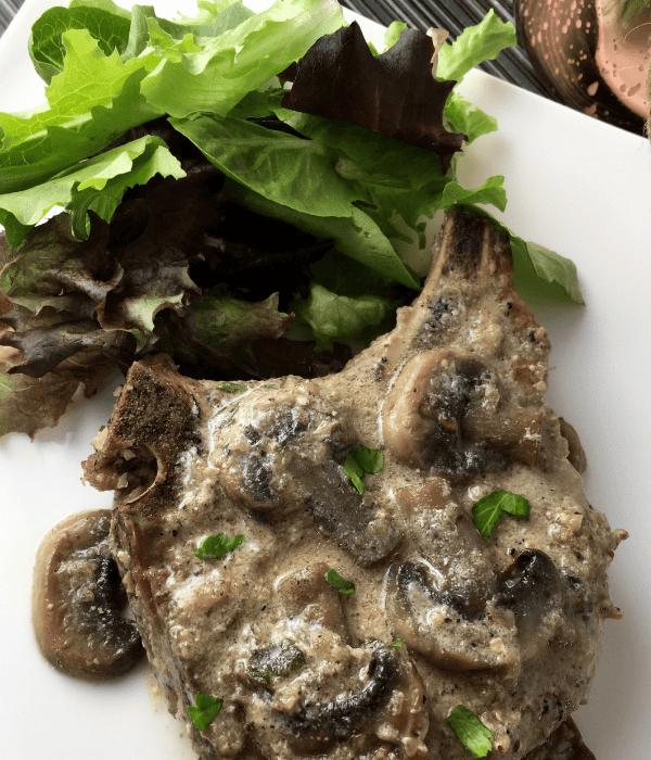 pork chops smothered with mushroom gravy with spring mix salad on white plate