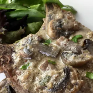 pork chops with gravy and mushrooms with spring mix greens on white plate