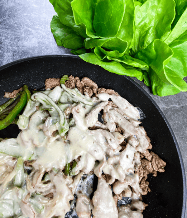 cast iron skillet with cheesesteak with green peppers and cheese with butter lettuce beside it