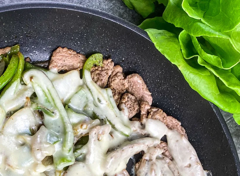 cheesesteak wrap mixture in cast iron pan with lettuce beside it